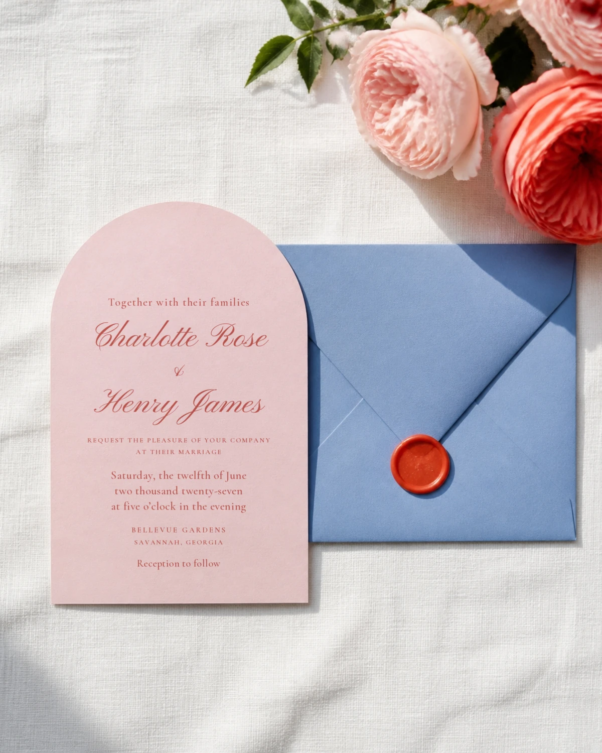 An arched blush wedding invitation for Charlotte Rose and Henry James in coral ink, beside a periwinkle envelope sealed at the flap with a coral wax seal